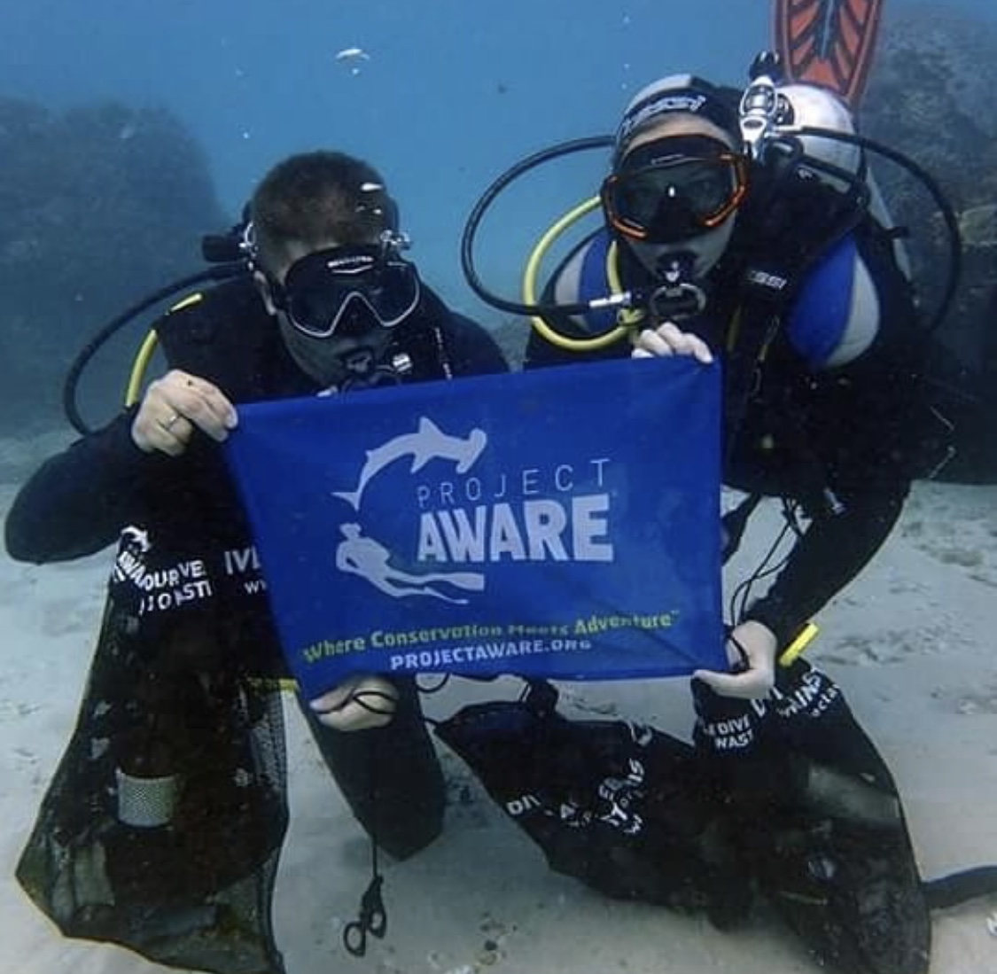 Divers with Project AWARE banner underwater