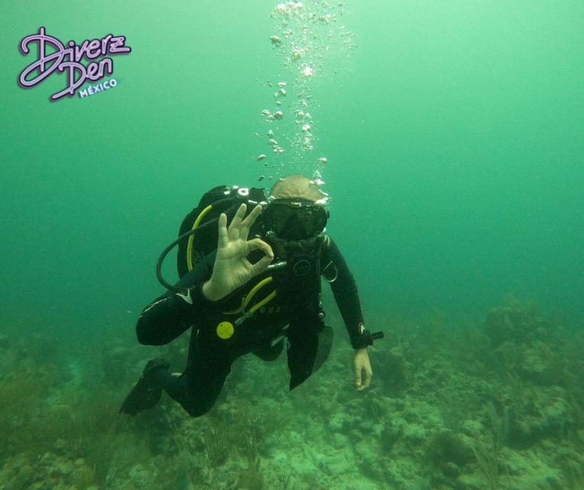 Divemaster Jorge making an OK sign to the camera while swimming over the reef.