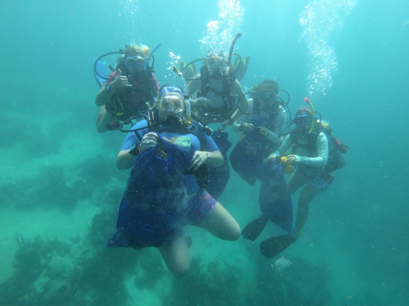 divers posing with mesh bags full of trash underwater