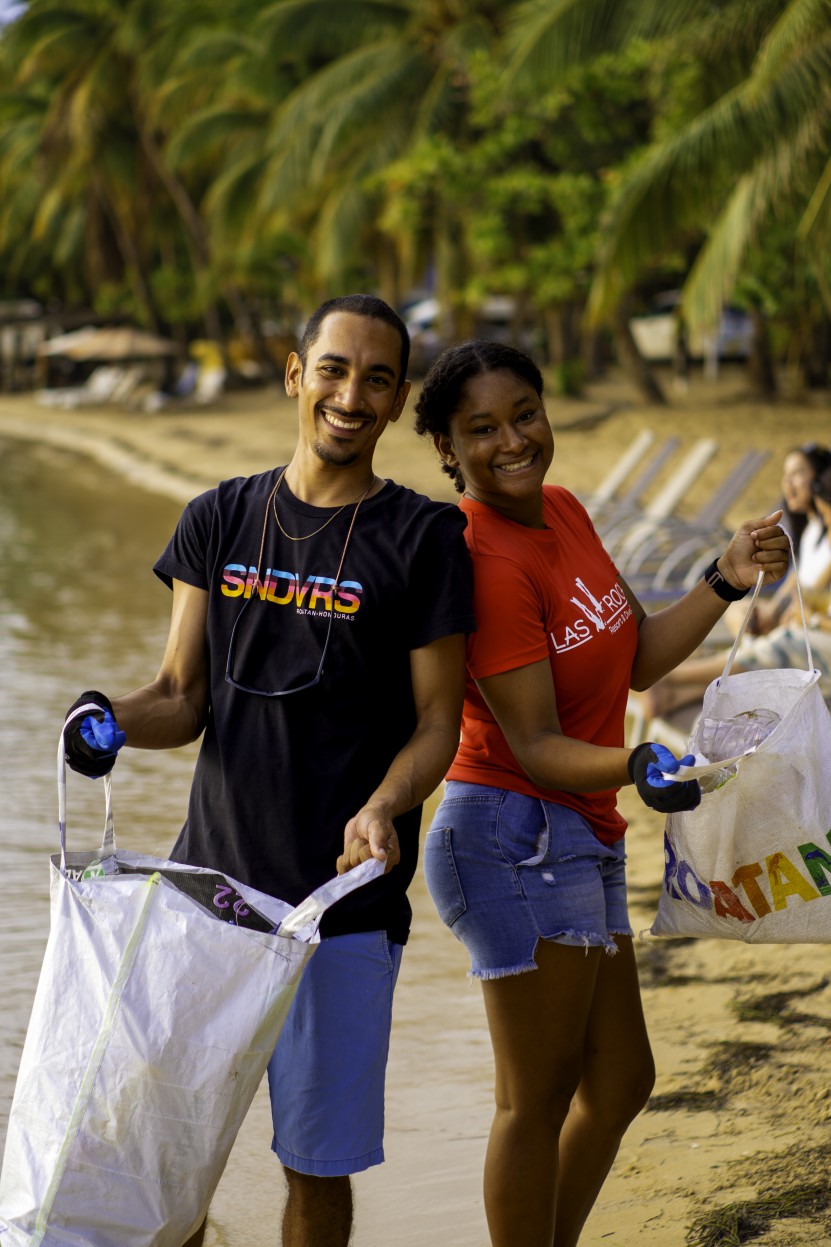 A man and woman hold up trash bags while participating in a beach clean up. 