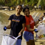 A man and woman hold up trash bags while participating in a beach clean up. 